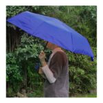Persona sosteniendo paraguas automático azul en jardín con fondo verde, ideal para lluvia o sol