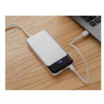 Power bank blanco con pantalla digital conectada por USB a laptop, muestra nivel de carga en tiempo real