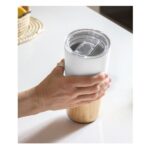 Mano sosteniendo vaso térmico blanco con base de bambú