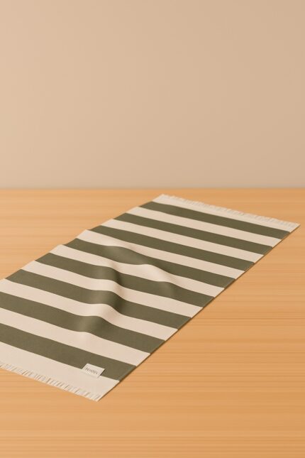 Lona rayada verde y beige con pliegues naturales sobre fondo beige y superficie de madera clara