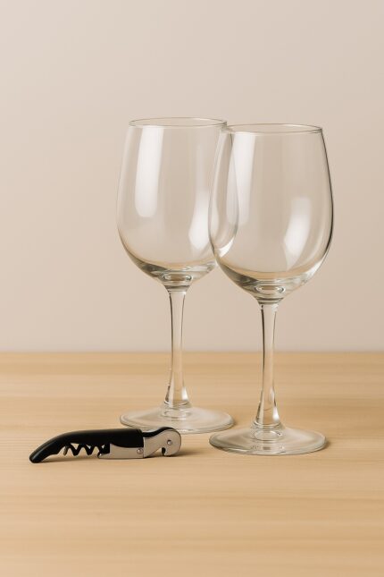 Dos copas de vino con abridor metálico sobre superficie de madera clara y fondo beige, set de regalo corporativo MQM.